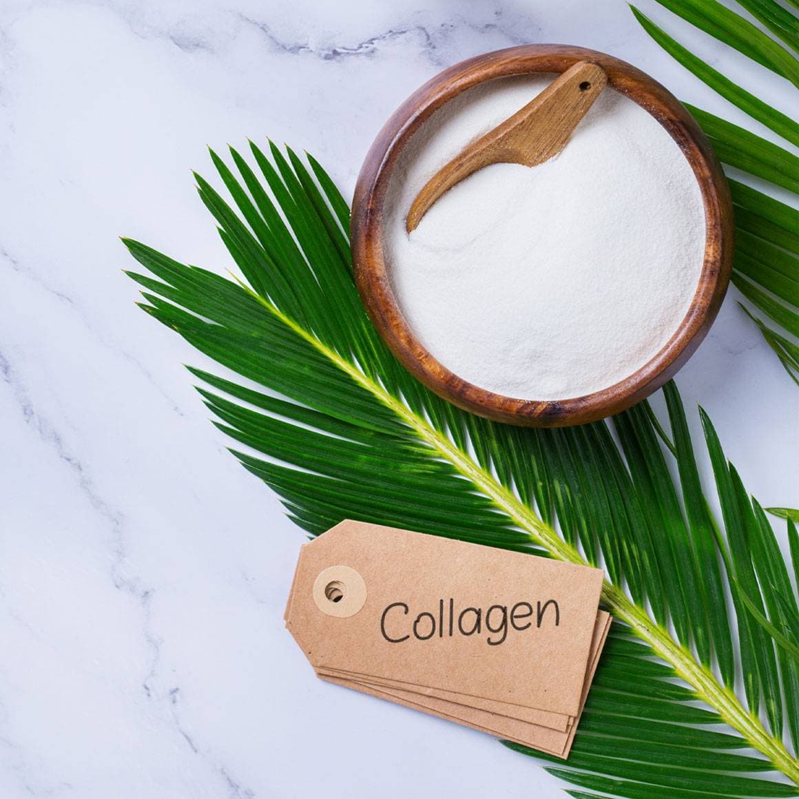 Колаген на прах в дървена купичка, до палмов лист и табелка с надпис Collagen