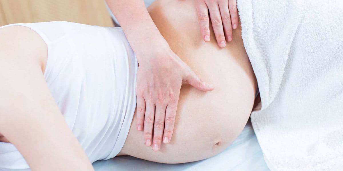 Blaga masaža stomaka trudnice koja leži na strani, pokrivena belim peškirom