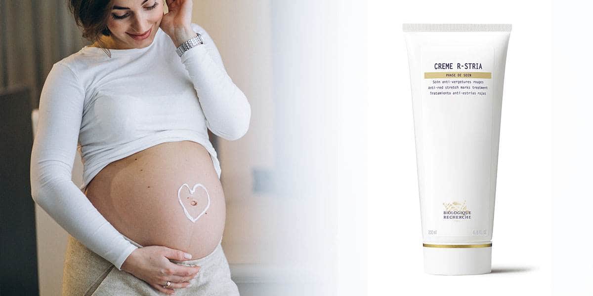 Бременна жена нанася крем върху корема си, до нея туба Biologique Recherche Creme R-Stria против стрии
